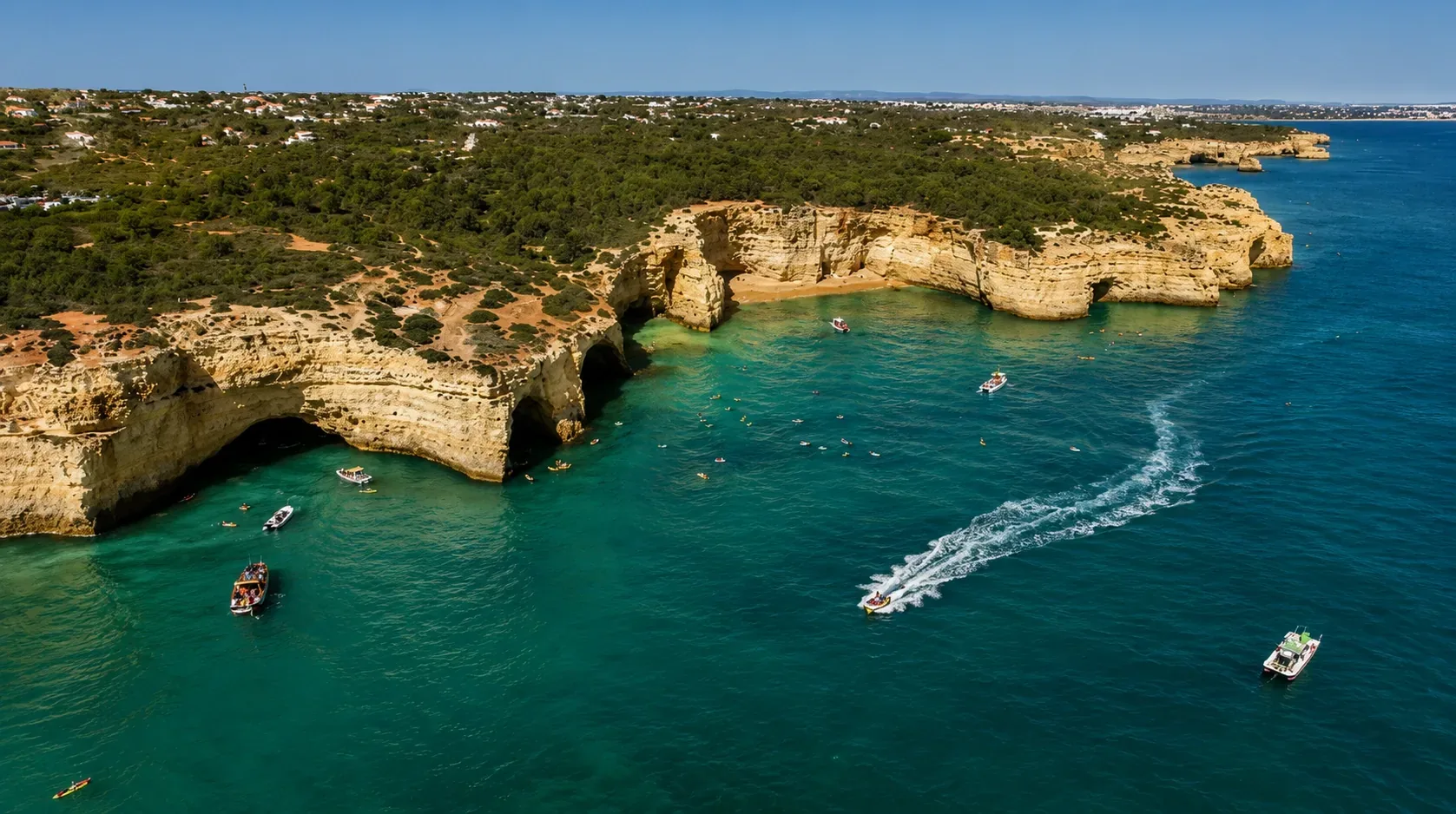 Golden limestone sea cliffs and rock arches along the Algarve coast near Benagil — turquoise Atlantic water and sculpted sandstone formations seen from a small boat, central Algarve, Portugal