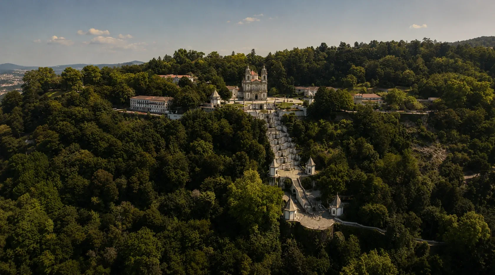 Full panoramic view of the UNESCO Bom Jesus do Monte Sanctuary in Braga — the complete baroque staircase of 583 steps climbing 116 metres through a forested hillside, with the neoclassical church at the summit, surrounded by woodland, the ornamental stairways with their fountains and statuary visible in the centre of the composition