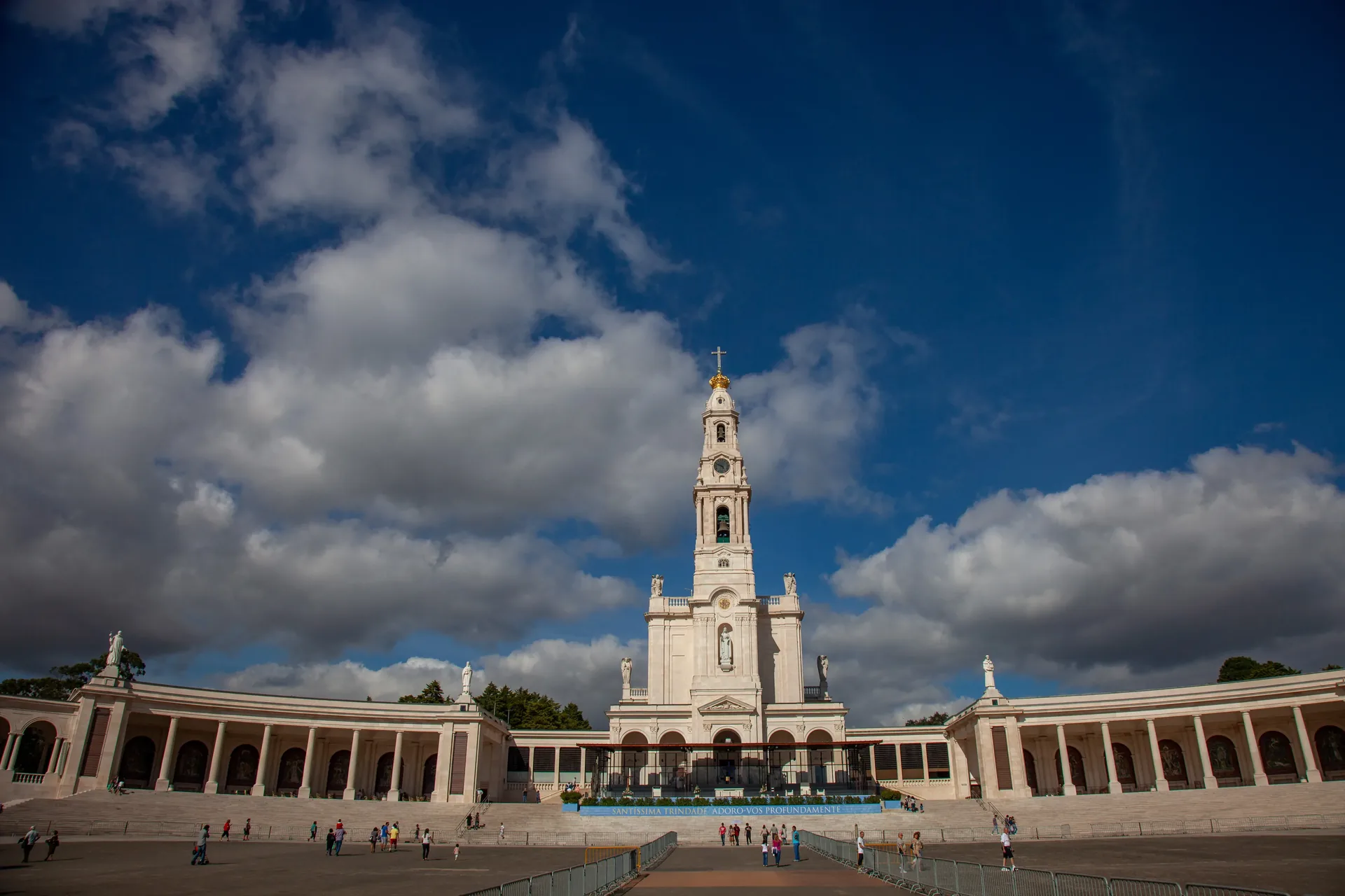 Wide view of the Fátima Sanctuary esplanade looking towards the Basilica of Our Lady of the Rosary — the immense open square flanked by colonnades, with pilgrims gathered, one of the world's most visited Catholic pilgrimage sites