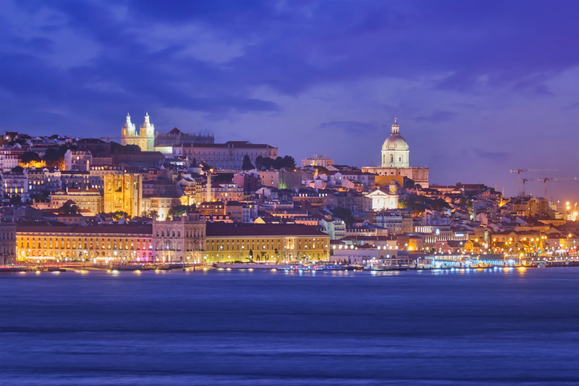 Narrow cobblestone lane in Alfama at dusk, lined with traditional tiled facades and warm lamplight