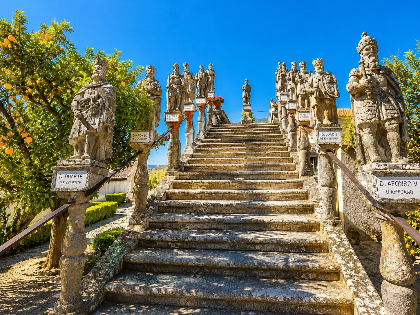 Stone baroque statues lining the garden staircase of the Jardim do Paço Episcopal in Castelo Branco — 18th-century granite figures of apostles and saints on the double staircase balustrades, weathered and mossy, a striking ensemble of Portuguese baroque garden sculpture