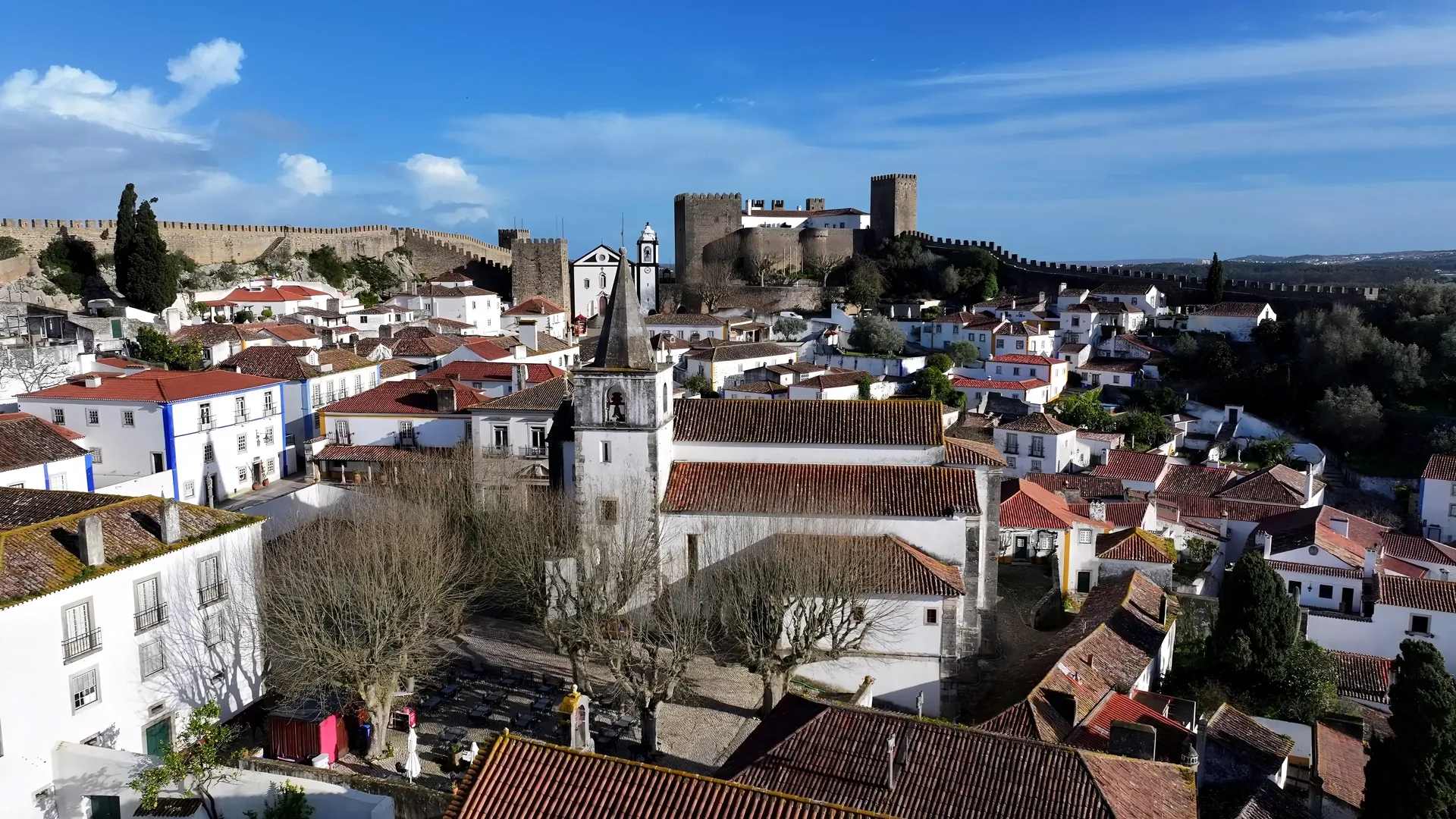 The intact medieval rampart walls of Óbidos enclosing the whitewashed village below — a perfectly preserved 14th-century fortified town available as a complimentary route stop on the return from Alcobaça to Lisbon
