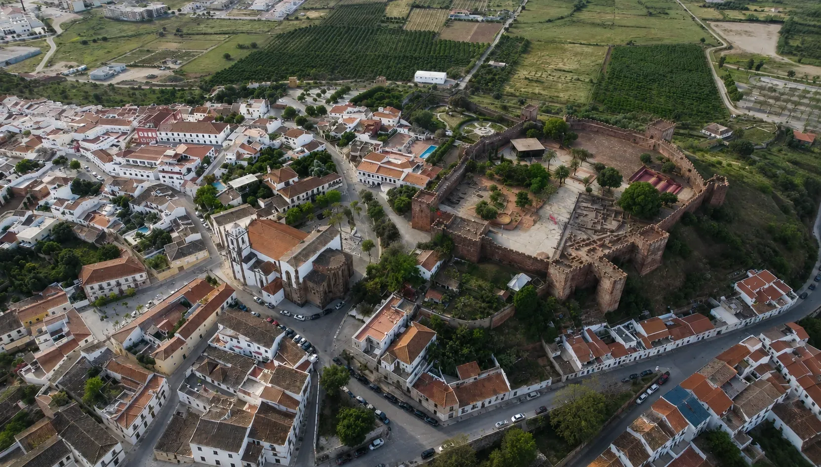 Gothic Cathedral of Silves with warm red sandstone facade in the historic centre of Silves — built on the site of the former Moorish Great Mosque, with the castle battlements visible on the hill above