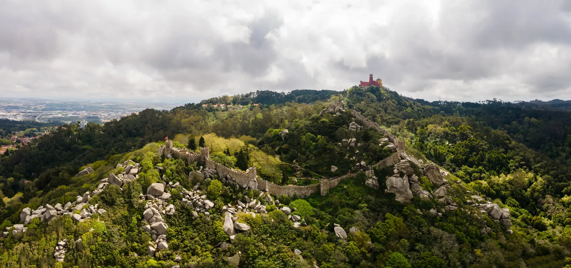 The Moorish Castle battlements stretching across the forested ridgeline of Serra de Sintra — the 8th-century hilltop fortress reconquered by King Afonso Henriques in 1147, offering panoramic views over Sintra village, the Atlantic coast, and Lisbon