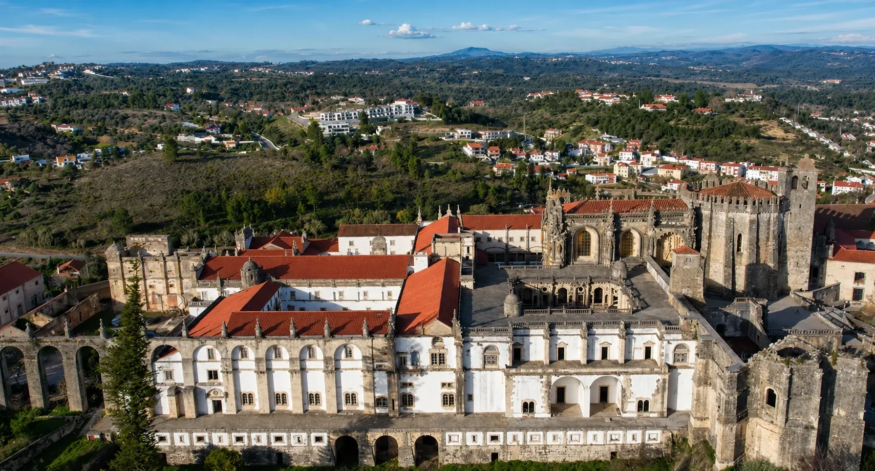 The exterior of the Convento de Cristo in Tomar — the UNESCO World Heritage fortified convent founded by the Knights Templar in 1160, with the Romanesque Charola rotunda and medieval defensive towers rising above the hilltop forest